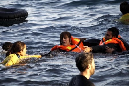 A volunteer lifeguard helps a refugee as a half-sunken catamaran carrying around 150 refugees most of them Syrians arrives after crossing part of the Aegean sea from Turkey on the Greek island of Lesbos