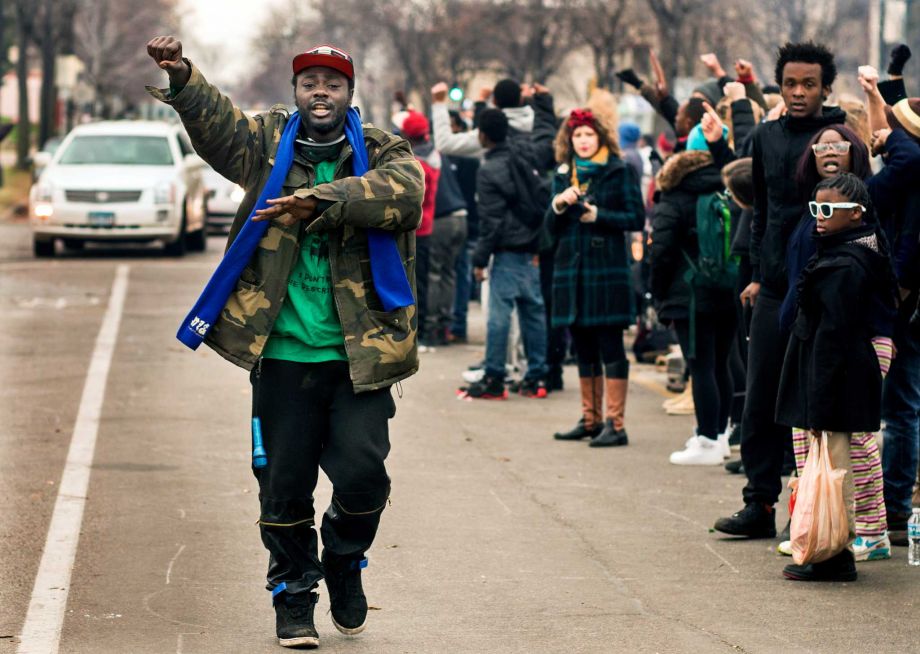 Demonstrators outside the Minneapolis Police Department’s 4th Precinct gesture as the the funeral procession for Jamar Clark passes by Wednesday Nov. 25 2015 in Minneapolis. Clark whose death in a confrontation with police has sparked more than