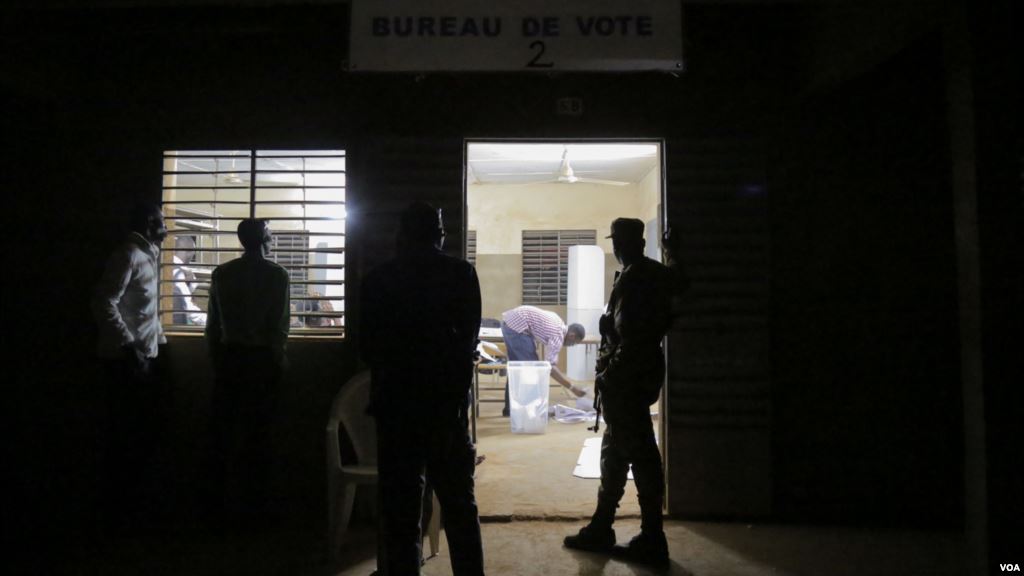 A guard and several bystanders are seen outside as votes are being counted at a polling station in Ouagadougou Burkina Faso