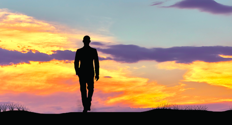 Silhouette of man walking alone at sunset