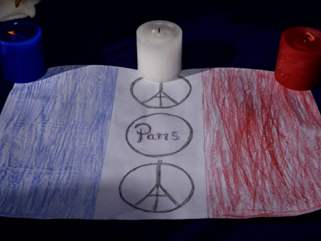 Red white and blue candles are displayed with a drawing of the French flag during a remembrance service in Civic Square Wellington