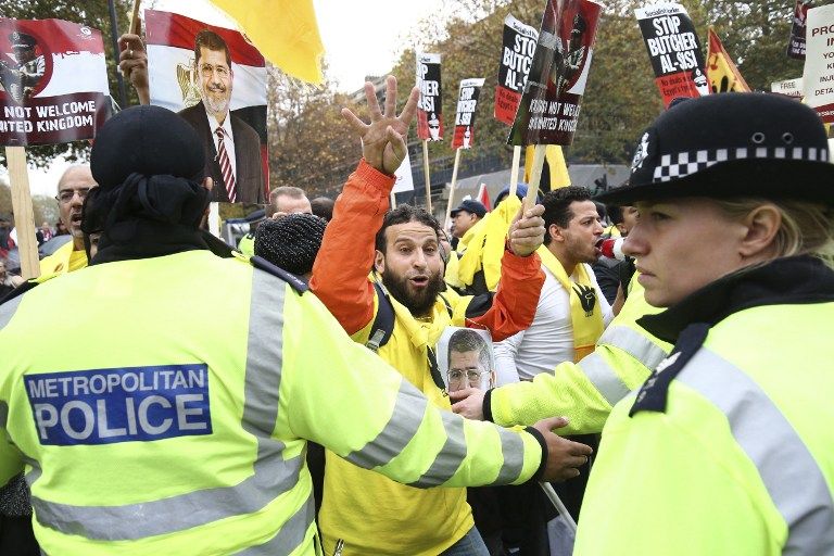 A protester flashes the four finger'Rabaa symbol as others hold placards some featuring the face of ousted Egyptian president Mohamed Morsi outside Downing Street in central London. – AFP pic