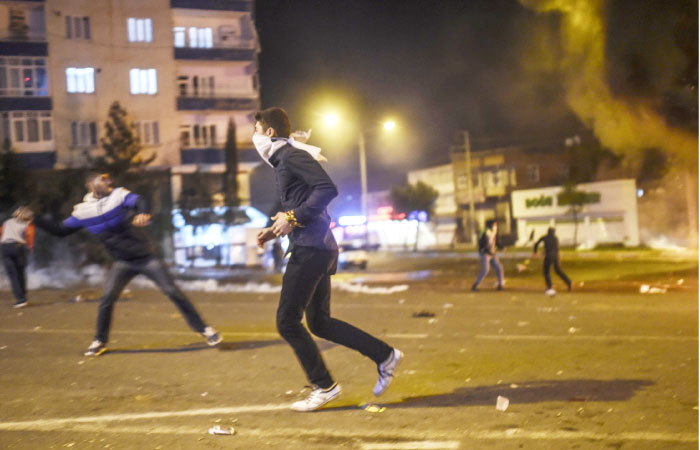 A man runs as others throw stones toward riot police during clashes between Turkish riot policemen and Kurdish protesters in the southeastern city of Diyarbakir on Sunday. — AFP