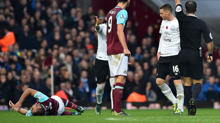 Everton's James Mc Carthy is booked while Dimitri Payet lies injured on the Upton Park pitch