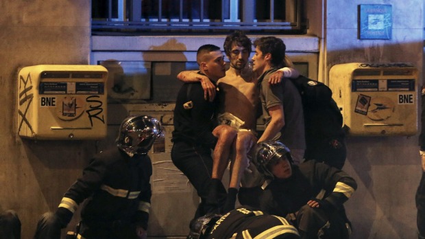 French fire brigade members aid an injured individual near the Bataclan concert hall following fatal shootings in Paris on Friday