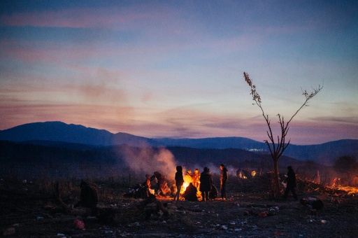 Migrants and refugees keep warm around a bonfire as they wait to enter a registration camp after crossing the Greek Macedonian border near Gevgelija