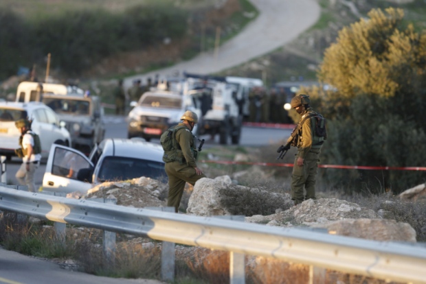 Israeli soldiers stand at the scene of the shooting of a rabbi and his son near the West Bank city of Hebron