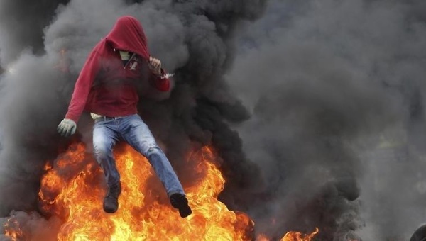 A Palestinian protester jumps over burning tires during clashes with Israeli troops near the Jewish settlement of Bet El near the West Bank city of Ramallah Oct. 26 2015