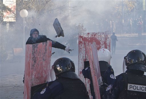 A supporter of the opposition parties in Kosovo throws a rock towards police in riot gear securing Kosovo's parliament building in capital Pristina on Tuesday Nov. 17 2015. Kosovo opposition used tear gas and pepper spray inside parliament and pel