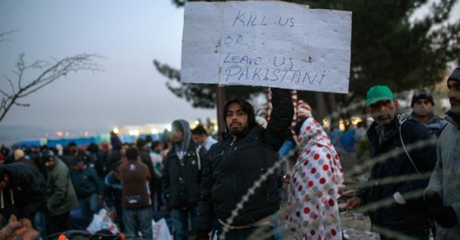 A migrant from Pakistan holds a placard as he waits with other migrants and refugees to cross the Greek Macedonian border near Gevgelija