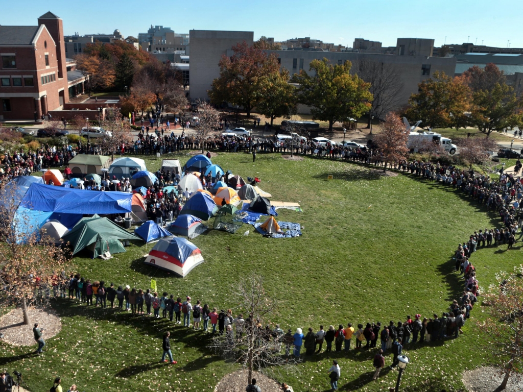 University of Missouri students circle tents on the Carnahan Quadrangle locking arms to prevent media from entering the space following the resignation of President Timothy Wolfe on Monday