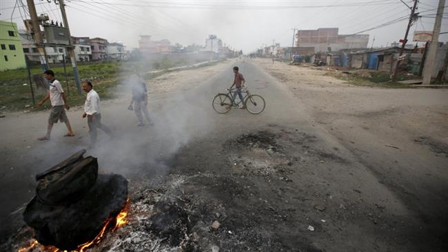 People walk near a burning tire on the highway connecting Nepal to India during an anti-constitution protest called by the Madhesi community in Birgunj Nepal