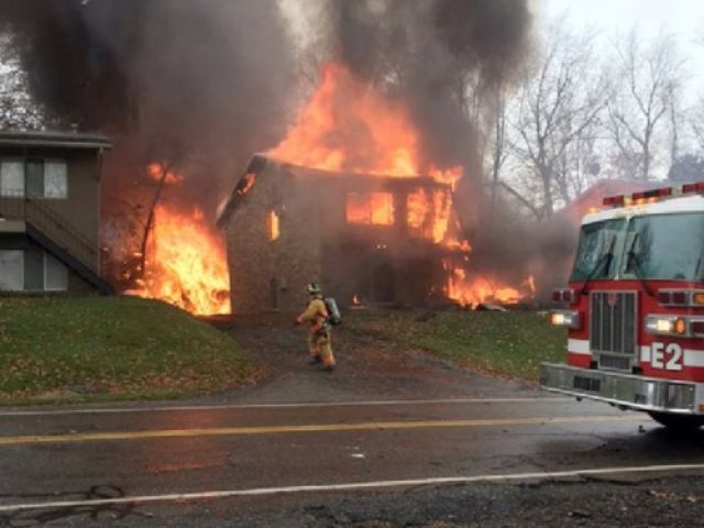 A firefighter walks up a driveway as an apartment building burns in Akron Tuesday where authorities say a small business jet crashed. The plane burst into flames and disintegrated after impact