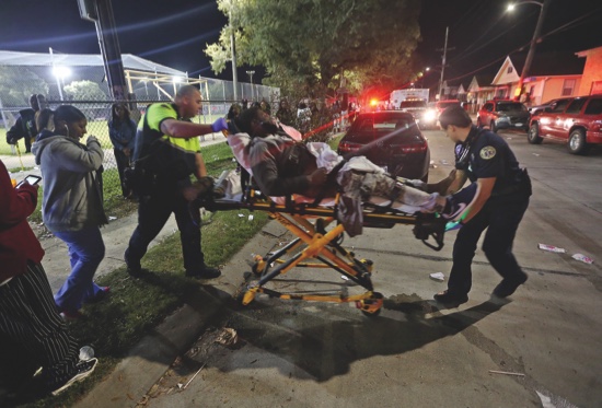 Officials remove a man from the scene following a shooting in New Orleans’ 9th Ward