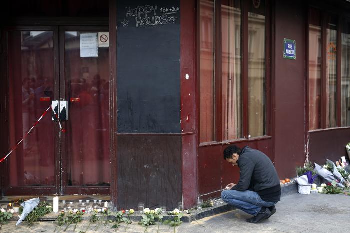 A man places a candle in front of the Carillon cafe in Paris Saturday Nov. 14 2015 a day after over 120 people were killed in a series of shooting and explosions