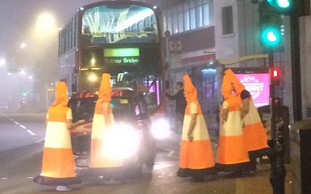 Men dressed as orange cones hold up traffic