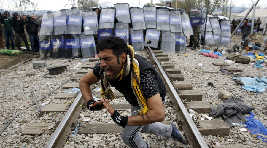 A stranded migrant reacts in front of a Macedonian police cordon as they clash after a migrant was injured when he climbed on top of a train wagon near the village of Idomeni Greece