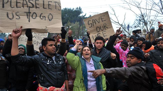 Refugees hold placards as they wait to cross the border between Greece and Macedonia near the Greek village of Idomeni