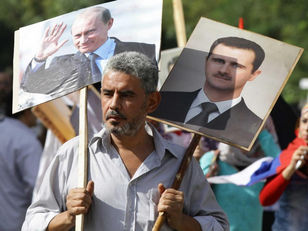 Syrian man hold placards bearing images of Vladimir Putin and Bashar al-Assad