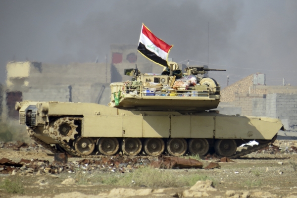 A national flag waves on an Iraqi Army Abrams tank as Iraqi forces supported by U.S.-led coalition airstrikes advance their position during clashes with Islamic State group in the western suburbs of Ramadi Iraq on Nov. 21 2015