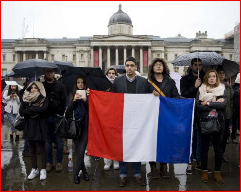 People hold a French national flag in front of the National in London today to pay tribute those killed in multiple attacks in Paris yesterday