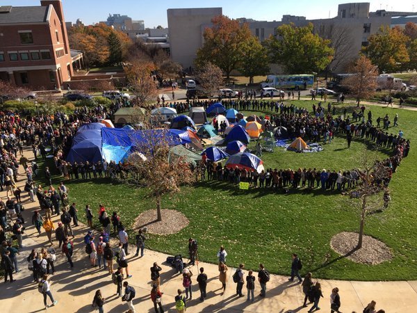 Students and faculty members form a circle around a campsite occupied by protesters at the University of Missouri