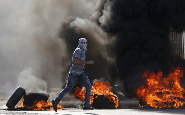 A Palestinian protester runs in front of burning tires during a clash with Israeli security forces. One Palestinian was killed in the protest