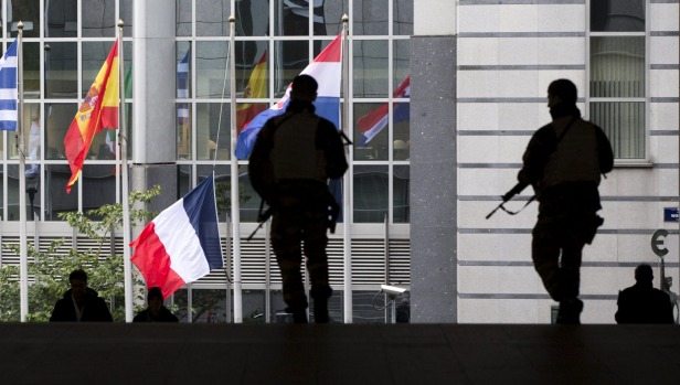 Armed soldiers stand guard outside the European Parliament where the French flag hangs at half mast after security level was raised in Belgium following the fatal shootings in Paris