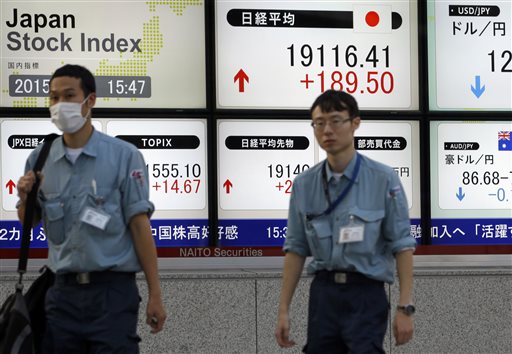 Workers walk past an electronic stock indicator showing the Nikkei 225 was up 1 percent at 19,116.41 in Tokyo Thursday Nov. 5 2015. Chinese stocks surged for a second day Thursday as confidence grew that stimulus measures are helping the world's N