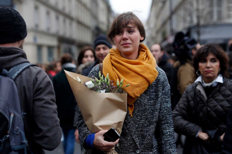 A woman carrying flowers cries in front of the Carillon cafe and the Petit Cambodge restaurant in Paris Saturday Nov. 14 2015 a day after a series of attacks in Paris. French officials said scores of people died Friday night when attackers launched