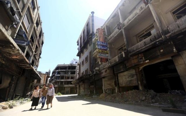 Women walk past damaged buildings along a street in the old city of Homs