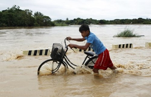 A boy pushes his bicycle through a flooded road after heavy rain at Candaba town Pampanga province north of Manila