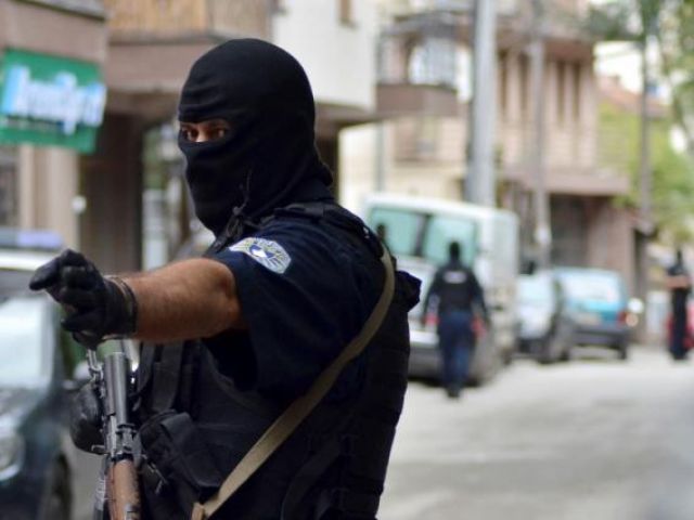 A masked police officer gestures as he stands guard in front of a court in Pristina