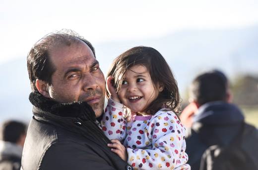 A migrant holds his daughter as they wait to enter the camp after crossing the Greek Macedonian border near Gevgelija