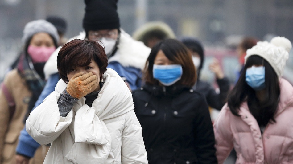 A woman uses her hand to cover her face from pollutants as people walk along a street on a polluted day in Beijing