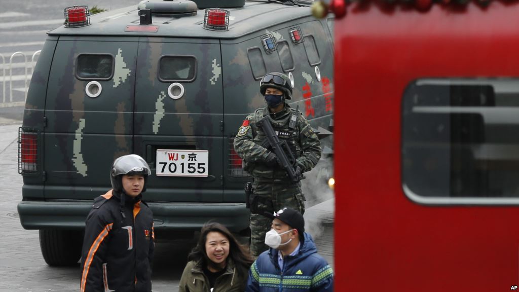 People walk past an armed Chinese paramilitary policeman standing guard in the capital city's popular shopping and nightlife area of Sanlitun in Beijing Dec. 27 2015