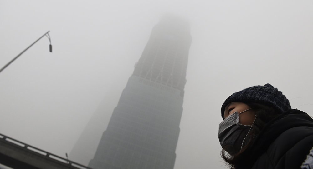 A woman waits for a bus below a skyscraper shrouded in smog on a heavily polluted day in Beijing