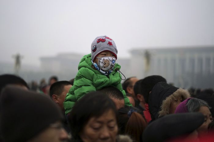 A boy wearing a mask sits on the shoulders of a man as they watch a flag-raising ceremony amid heavy smog at the Tiananmen Square after the city issued its first ever'red alert for air pollution in Beijing China