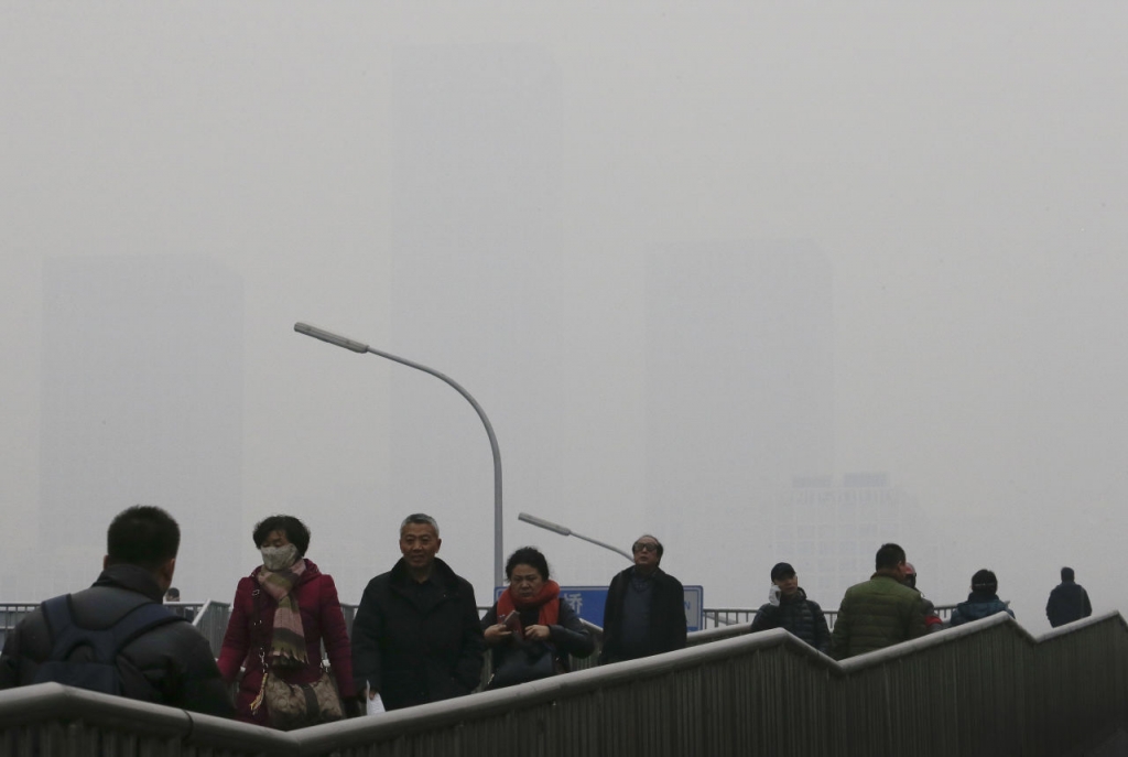 People walk on a pedestrian overhead bridge as office buildings in Central Business District of Beijing are shrouded with heavy haze Tuesday Dec. 8 2015. Beijing's red alerts for smog are as much about duration as they are about severity of pollution