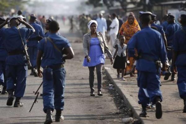 A woman passes by policemen during a protest against Burundi President Pierre Nkurunziza and his bid for a third term in Bujumbura Burundi