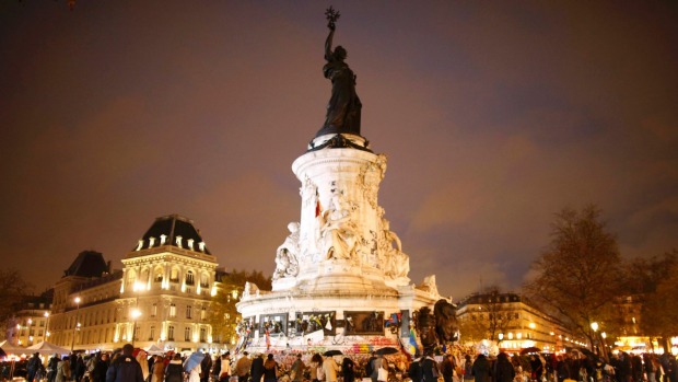 People share a quiet moment in front of flowers candles and messages at the Place de la Republique in Paris