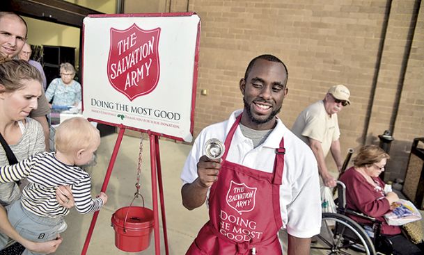 Jerel Jordon of Columbus rings a Salvation Army charity bell outside of Hobby Lobby during Black Friday. Jordon has been ringing each season since he was 16-years-old. Augustus Link 17-month-old is held over the bucket to put change in by his mother