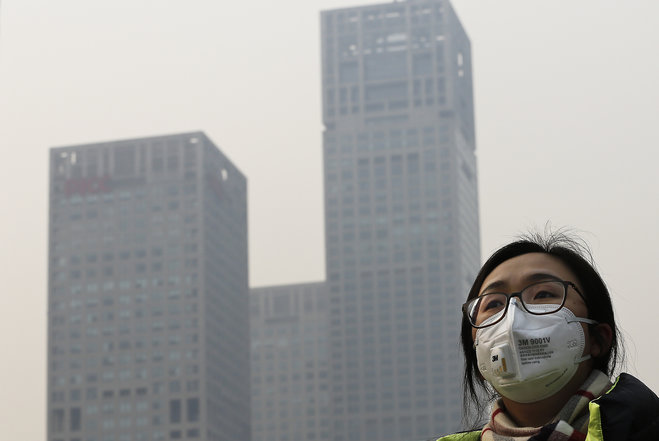 A woman wearing a face mask to protect herself from pollutants walks past office buildings shrouded with pollution haze in Beijing Monday Dec. 7 2015. Beijing issued its first-ever red alert for smog on Monday urging schools to close and invoking rest