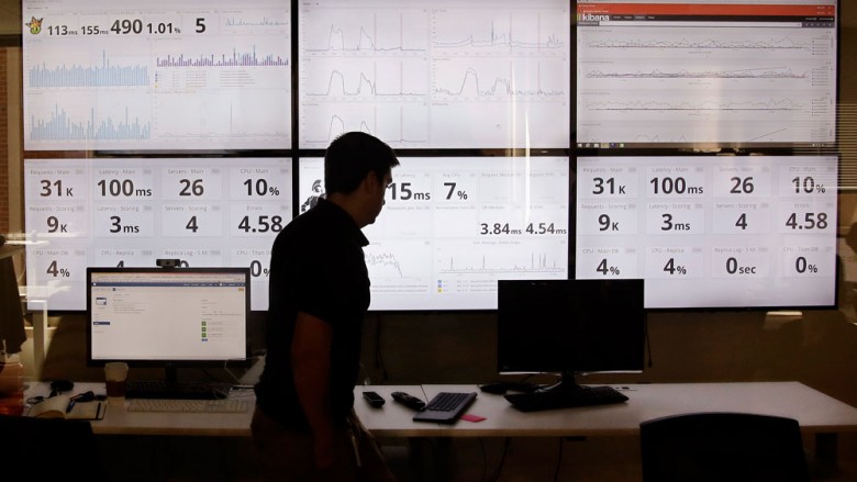 An employee in the software development department of DraftKings a daily fantasy sports company walks past screens displaying the company's online system stats in Boston