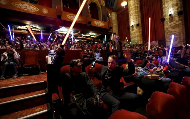 Moviegoers cheers and wave lightsabers before the first showing of the movie