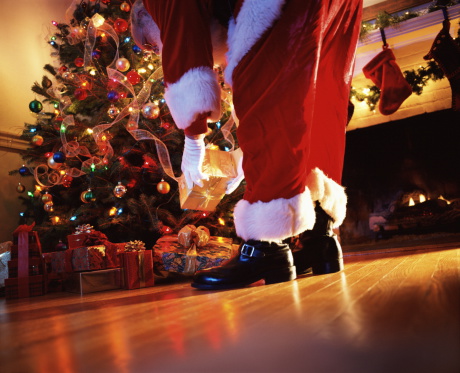 Santa Claus placing gift under tree