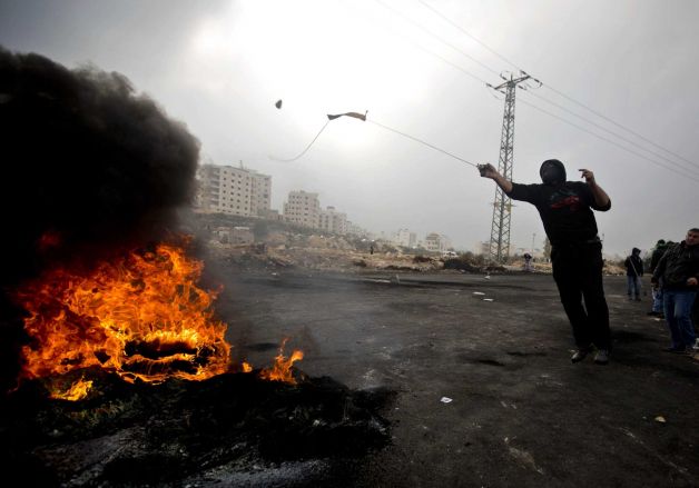 A Palestinian protester uses a sling shot to hurl stones at Israeli troops during clashes after the funerals of Ahmed Abu al-Aish 28 and Laith Manasrah 21 from Qalandia refugee camp in the West Bank city of Ramallah Monday Nov. 16 2015. Two Pales