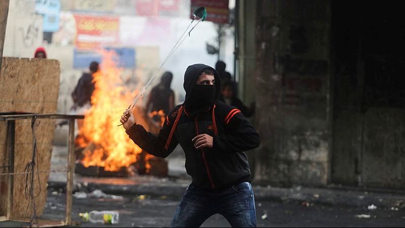 Palestinian protesters use slingshots to hurl stones towards Israeli troops during clashes in the West Bank city of Hebron