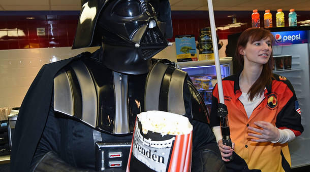 A Darth Vader cosplayer from The Twin Suns Star Wars Club serves popcorn to fans on opening night of Walt Disney