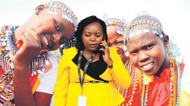 An usher uses her mobile phone next to a poster displaying Masai girls outside the Kenyatta International Conference Centre venue for the World Trade Organisation Summit in Nairobi Kenya yesterday